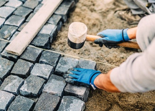 Albañil asentando adoquines de piedra con maza de goma siguiendo el hilo de replanteo