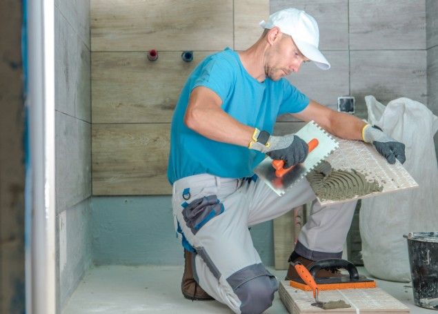 Alicatado de baño con llana dentada Alicatador aplicando cemento cola con llana dentada al dorso de un azulejo de baño