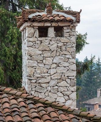 Chimenea de mampostería de piedra rematada con teja curva sobre el faldón de una cubierta