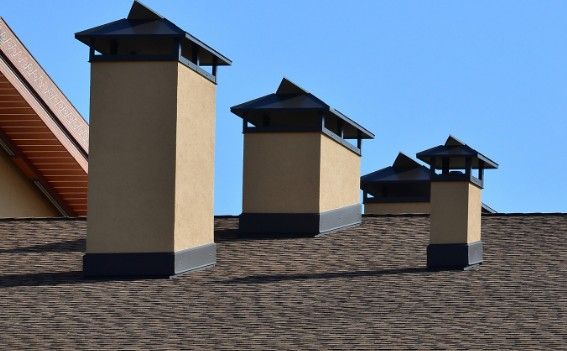 Cuatro conductos de chimenea revocados y rematados con sombrerete metálico sobre la cubierta
