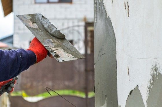 Enfoscado de pilastra con mortero Albañil aplicando mortero con la llana sobre la pilastra de un muro exterior
