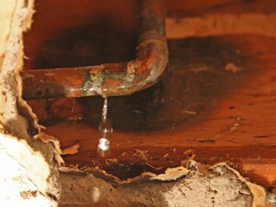 Fuga en una tubería empotrada Tubería de cobre corroída goteando dentro del forjado de madera abierto de una vivienda