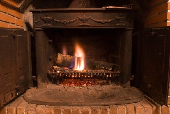 Hogar de chimenea de leña Hogar de chimenea de leña encendido, con frente de hierro fundido y jambas de ladrillo