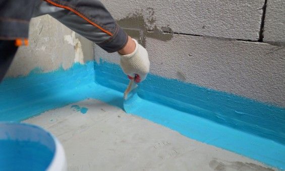 Impermeabilización líquida de encuentros y petos Operario aplicando con brocha membrana líquida azul en el encuentro entre la solera y el muro
