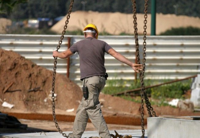 Izado de losa prefabricada con grúa Operario guiando con las cadenas de la grúa el izado de una losa prefabricada