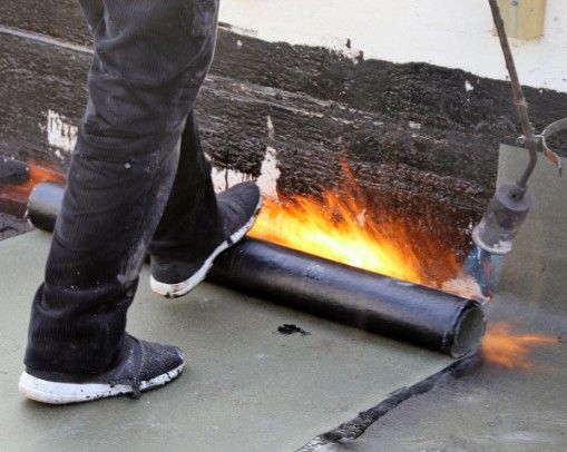 Soldadura de lámina asfáltica con soplete Operario soldando con soplete el rollo de lámina asfáltica sobre una cubierta plana